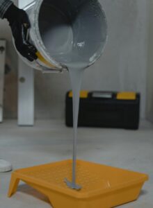Gray paint pouring into a yellow tray, ideal for room renovation projects.