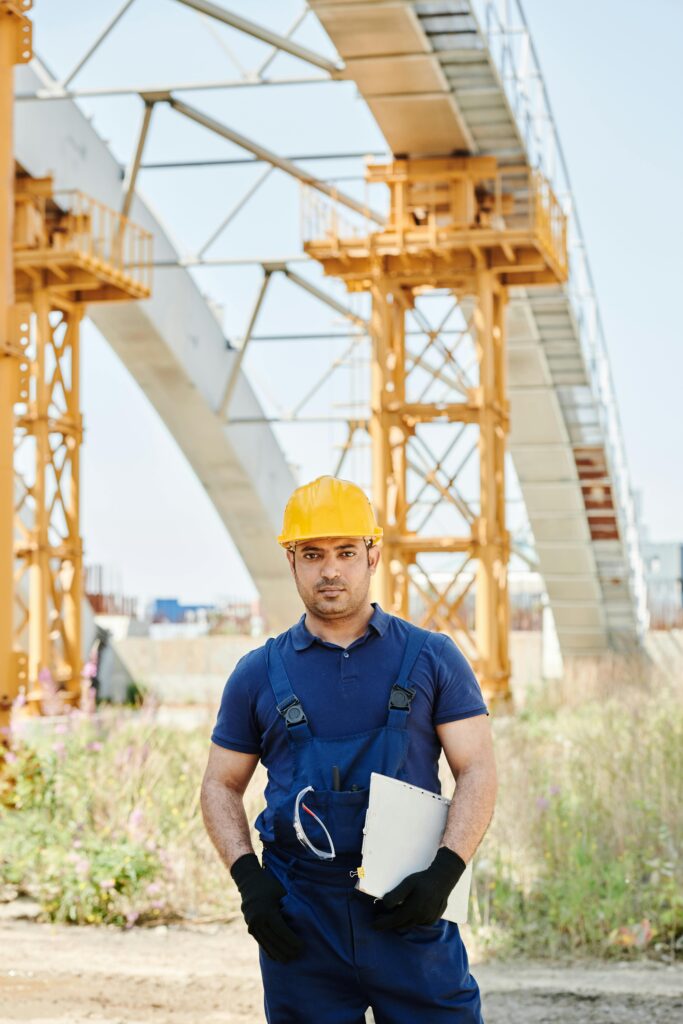 Engineer in safety gear holding a clipboard at a construction site with arches in the background.